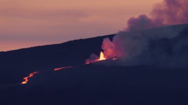 Mauna Loa volcano fountain eruption on Big Island, Hawaii USA 4K RED camera distance shot. Flowing red hot lava and craters. Dangerous thick fume smog raising up in air at cinematic rose gold sunset 