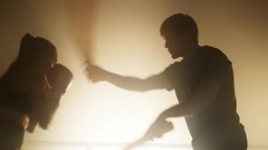 Close-up shot of a girl burning calories in a fitness centre. Portrait of female boxer in boxing gloves training with her professional coach with a spotlight in the background. High quality 4k footage