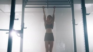 Portrait of a young, blonde-haired woman using pull up bar in the gym. Close-up shot of female athlete lifting her knees to the chest level while training her abs muscles. High quality 4k footage