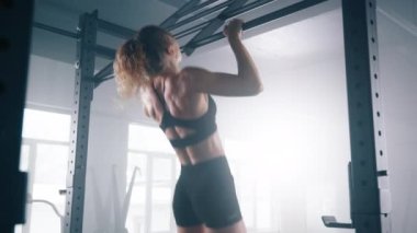 Portrait of a sportswoman practicing intensive workout. Close-up view of female athlete using pull up bar to build impressive upper-body muscle in loft-styled gym studio. High quality 4k footage