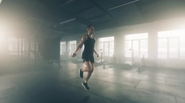 Close-up shot of dedicated, sporty guy in his 30s working out indoors. Portrait of a sportsman using a jumping rope to gain lean leg muscles in the gym. High quality 4k footage