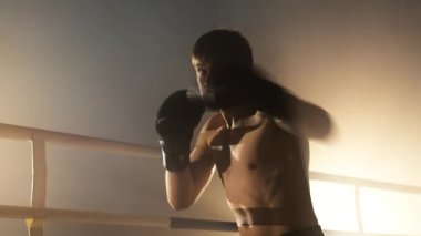 Close-up shot of male athlete training in boxing gloves indoors. Portrait of a handsome, healthy boxer warming up before intensive, tough sparring in the ring. High quality 4k footage