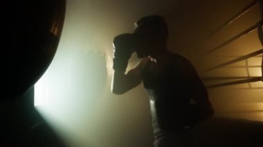 Close-up view of male athlete boxing with a bag in leather gloves while having a high intensity interval training. Portrait of aggressive, strong man building his muscles. High quality 4k footage