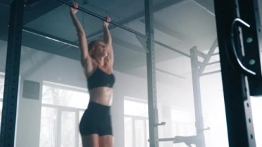 Close-up of caucasian sportswoman performing abs crunches to gain fit and healthy body. Portrait of a young, blonde-haired woman using pull up bar in the gym. High quality 4k footage