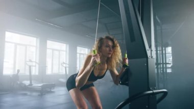 Close-up view of caucasian, blonde-haired female athlete having intensive workout. Portrait of slim and healthy woman looking focused while working on a fitness trainer. High quality 4k footage