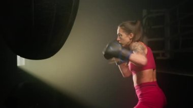 Close-up shot of experienced female boxer reducing her stress while punching a bag. Portrait of a beautiful, sporty woman with a tattoo on her arm working out. High quality 4k footage