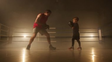 Portrait of confident, active kid sparring with a coach in boxing ring. Close-up of sporty boy punching in leather gloves to train his endurance. High quality 4k footage