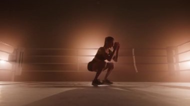 Portrait of young, caucasian woman in black sportswear squatting in boxing ring. Close-up view of female athlete performing lunges to build strong leg muscles. High quality 4k footage