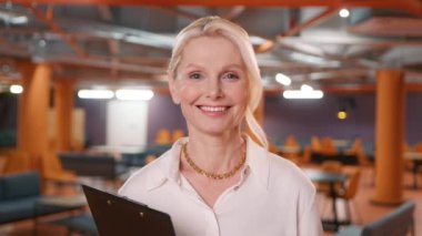Headshot successful lawyer looking at camera standing in office 4K. Portrait of happy smiling mature blonde businesswoman, small business owner, company leader or sales manager, female CEO executive