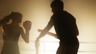 Portrait of female boxer in boxing gloves training with her professional coach with a spotlight in the background. Close-up view of skilled boxers working out in the ring. High quality 4k footage