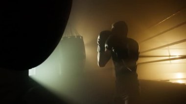 Portrait of aggressive, strong man building his muscles. Close-up view of caucasian sportsman having fitness boxing training in dark, modern gym club. High quality 4k footage
