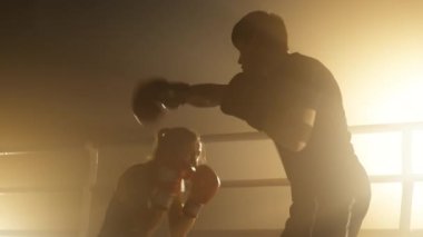 Portrait of sparring partners warming up before a match in boxing ring and spotlights around. Close-up shot of female athlete training with a coach indoors. High quality 4k footage