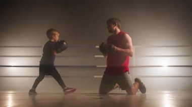 Close-up view of adult man standing on his knees and teaching a kid boxing. Portrait of caucasian sparring partners working out in sport ring together. High quality 4k footage