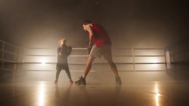 Boy punching and hitting his coach during intensive boxing fitness workout in empty gym studio. Close-up view of focused kid training with his father. High quality 4k footage