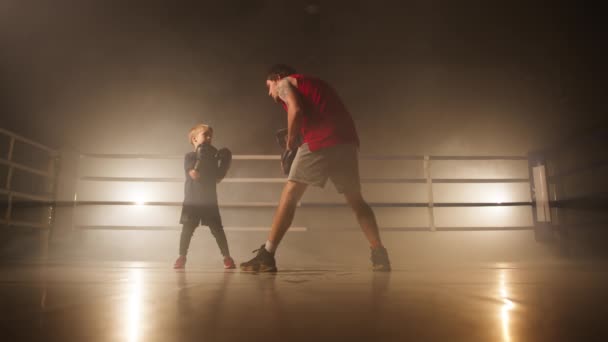 空のジムスタジオで集中的なボクシングフィットネスワークアウト中に少年パンチと彼のコーチを打つ 彼の父との集中的な子供の訓練のクローズアップビュー 高品質4K映像 — ストック動画