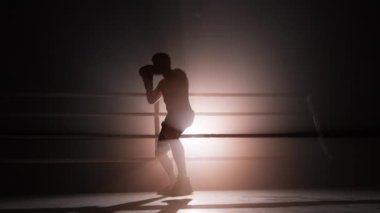 Close-up view of well-trained athlete with lean body warming up before a sparring. Portrait of unrecognizable man wearing boxing gloves and practicing a knock. High quality 4k footage