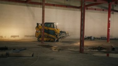 01 FEB. 2023. CALIFORNIA, USA. Footage of small track loader working in industrial hangar. Commercial machinery with switched on lighting operating factorys facilities. High quality 4k footage