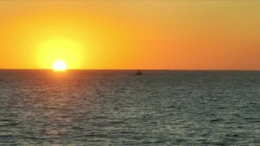 Drone shot of calm ocean at majestic golden hour as seen from the shore. Small vessels sailing across stunning, tranquil seascape below colorful skyline. High quality 4k footage