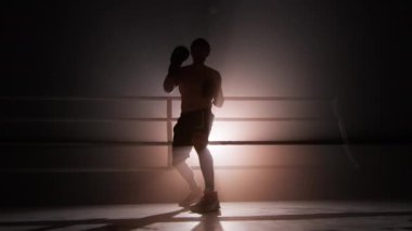 Portrait of unrecognizable man wearing boxing gloves and practicing a knock. Close-up shot of male boxer boosting whole-body strength with a spotlight in the background. High quality 4k footage