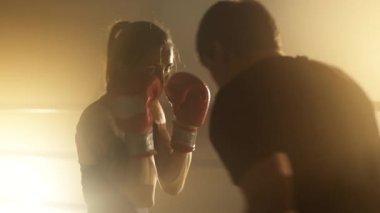 Portrait of a woman having tough, intensive workout with her male coach indoors. Close-up view of caucasian girl practicing her punch in boxing gloves. High quality 4k footage