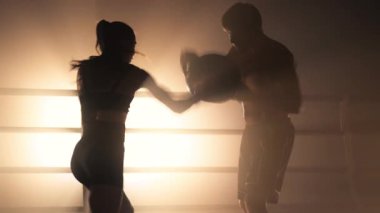 Sporty couple building muscle strength and burning calories in the gym. Close-up view of aggressive woman in boxing gloves punching her coach during a tough workout. High quality 4k footage