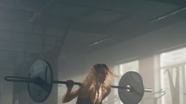 Close-up shot of a sportswoman performing weighted squats in the gym. Portrait of strong, experienced bodybuilder holding heavy barbell on her shoulders. High quality 4k footage
