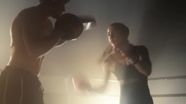 Close-up shot of male and female athletes punching and kicking while training. Portrait of a woman training with her coach with a spotlight in the background. High quality 4k footage