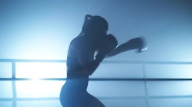 Portrait of determined, female kickboxer training her punch. Close-up view of a young woman practicing her attack and warming up before a sparring in the boxing ring. High quality 4k footage
