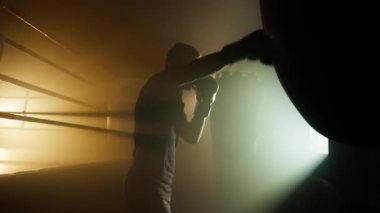 Close-up view of caucasian sportsman having fitness boxing training in dark, modern gym club. Portrait of active, young athlete improving his health and strength. High quality 4k footage