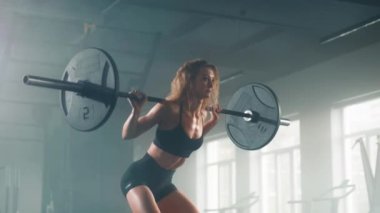 Portrait of active and motivated girl training her lower body indoors. Close-up shot of a sportswoman performing weighted squats in the gym. High quality 4k footage