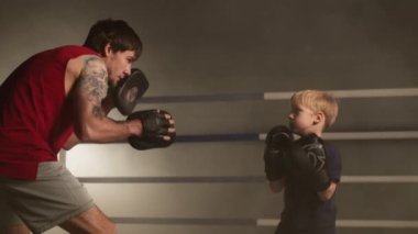 Portrait of a man teaching little boy in boxing gloves how to kick and punch. Close-up of young and adult sparring partners looking focused and motivated. High quality 4k footage