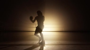Close-up shot of a sportsman in boxing gloves training in the boxing club to burn calories. Portrait of young and healthy kickboxer working out in empty gym club. High quality 4k footage