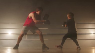Little boy looks skilled and strong while training with his boxing coach. Close-up shot of a kid in gloves sparring with adult boxer in a ring. High quality 4k footage