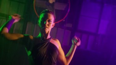 Lonely dramatic woman is getting wet under rain in darkness, standing under streams of water in purple green spotlights with futuristic grunge studio on background. Slow motion seductive erotic dancer