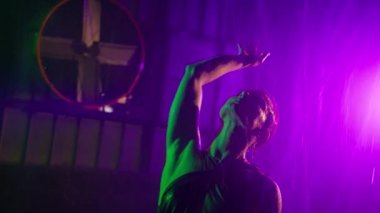 Flirting girl looks seductively in wet outfit caressles touching herself. Silhouette of sexy woman dancing under rain in glowing led pink purple light on cyberpunk futuristic grunge studio background