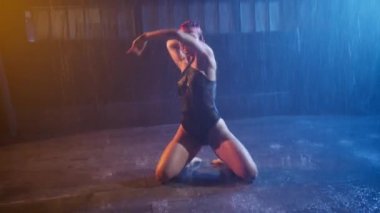 Hot sexy woman splashes hair in water creating splashes. Silhouette of young slender body in wet underwear body suite. Seductive female poses under rain, dark grunge futuristic urban studio background