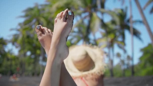 ブルーペディキュアで女の足を塞ぐRedカメラで撮影 緑のヤシの木がある黒い砂浜でリラックスした幸せな女性の足 暑い夏のエキゾチックなハワイ島での認識できない女性 — ストック動画