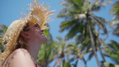 Beautiful woman wearing straw hat and red bikini on a paradise exotic island enjoying journey, summer vacation on Hawaii island, USA tourism concept, tourism with green palms background RED camera 4K