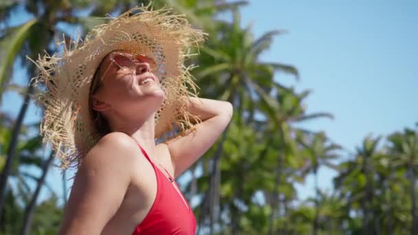 スローモーションビーチのコンセプト 緑のヤシの木の背景を持つビーチでわら帽子の笑顔の女の子 光の潮風を楽しむ エキゾチックな島で夏休み ハワイのビーチでの休暇 — ストック動画