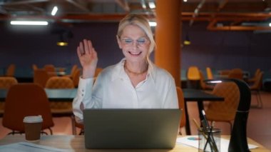 Olgun iş kadını şık gözlükler takıyor web kamerasına konuşuyor uzaktan video konferans görüşmesi yapıyor. Kadın mesai saatleri dışında mesai saatleri dışında uluslararası sohbetler yapıyor.