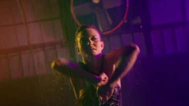 Woman dancing hot dance under rain. Professional dancer in wet bodysuit performs dance movement by hands. Closeup studio shot of female artist dancing inside dark place. Dance art concept footage