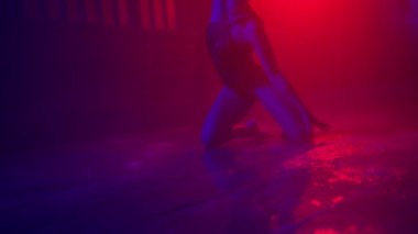 Silhouette of professional go go dancer in black bodysuit dancing flexible in darkness under a theatrical rain drops and red spotlights of studio flashing on background. Slow motion sexy dance on RED