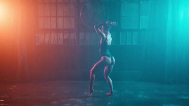 Beautiful sexy woman in bodysuit or swimwear dancing in garage urban space in rain. Sensual scene of female model doing different sexy movements on wet floor with water splashes. Erotic performance 4K