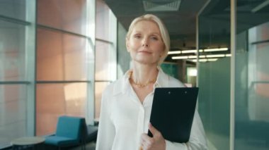 Kapalı portre, koridorda yürüyen olgun, kendine güvenen 50 'li yaşlarda bir kadın. Ciddi bir iş kadını iş merkezinin koridorunda klasörle geziyor. İş kadını portresi ofis koridorunda 4K kamerasına bakıyor.