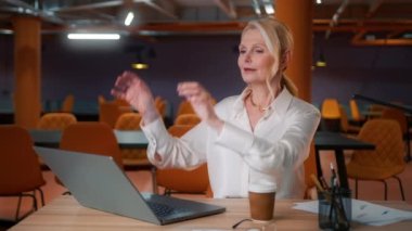 Olgun odaklı kadın yönetici iş kadını masa başında oturuyor çağdaş şirket ofisinde dizüstü bilgisayarda yazı yazıyor, sandalyeye yaslanıyor. İş teknolojileri konsepti 4K