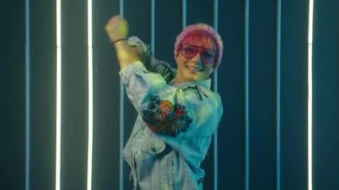 Moda tutkunu genç kadın vlogger müzik dinliyor, dans ediyor ve sosyal medya için video kaydediyor. Light Wall 'daki gece kulübünde disko dansçısı. tiktok uygulaması kullanılarak dans videosu oluşturuluyor. 