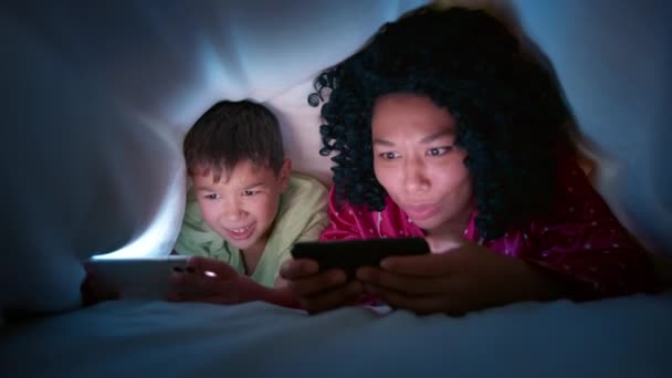 담요로 침대에 디지탈 스마트폰 기술을 사용하는 호기심많은 아동이다 전화로 온라인 — 비디오