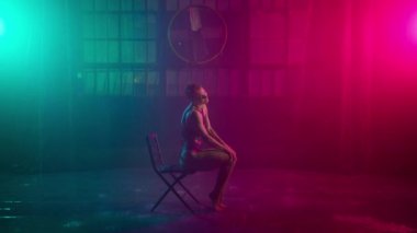 Esnek kız gece kulübünde sandalyede jimnastik striptiz yapıyor. Genç seksi dansçı ıslak dans pistinde yağmur altında sandalyede sicim yapıyor. Güzel kadın renkli spot ışıkları altında dans ediyor