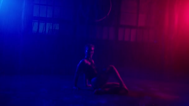 サイバーパンク スタジオで雨の下で踊るセクシーな女性 美しいです体を持つ誘惑女性プロダンスオンぬれた床で青と赤の光とともにホワイトストロークで暗いスタジオで水のスプラッシュ — ストック動画