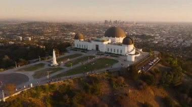 Tepedeki Griffith Park gözlemevi etrafındaki destansı günbatımı anteninde Los Angeles şehir merkezindeki hareketli arka planda güneş ışınları mercekleri parlıyor. Los Angeles Seyahat Varış Yeri 4K LOS ANGELES, ABD Şubat 2023